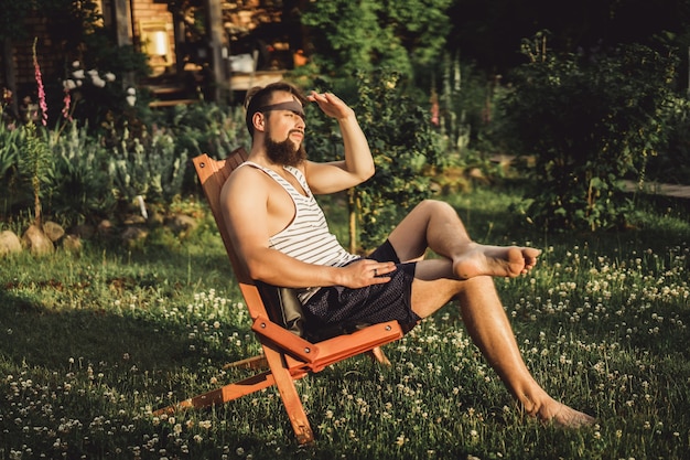 un homme se repose dans une maison de campagne. Un homme barbu apprécie le coucher de soleil sur une pelouse verte.