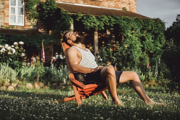 un homme se repose dans une maison de campagne. Un homme barbu apprécie le coucher de soleil sur une pelouse verte.