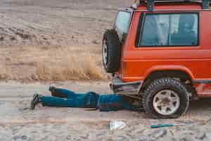 Photo gratuite l'homme se trouve sous une voiture 4x4 sur un chemin de terre