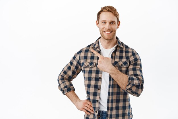 Homme séduisant et confiant aux cheveux roux et à la barbe pointant le doigt dans le coin supérieur gauche montrant une nouvelle offre de boutique promotionnelle démontrant un texte promotionnel debout sur fond blanc