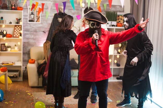 Homme séduisant habillé comme un pirate faisant du karaoké à la fête d'halloween avec ses amis.