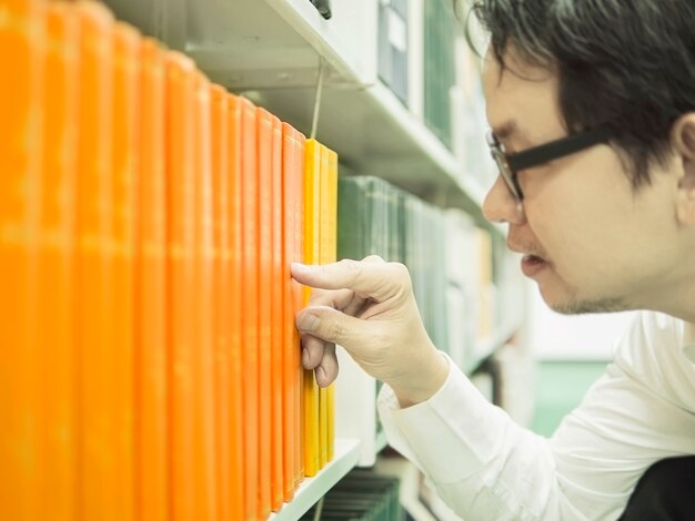 L&#39;homme sélectionne le livre d&#39;une étagère dans une bibliothèque