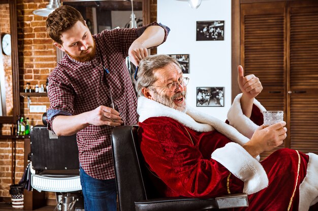 L'homme senior en costume de père Noël raser son maître personnel au salon de coiffure avant Noël