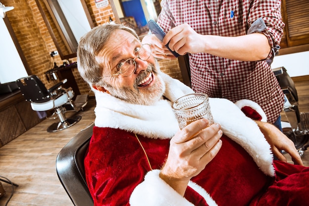 L'homme senior en costume de père Noël raser son maître personnel au salon de coiffure avant Noël