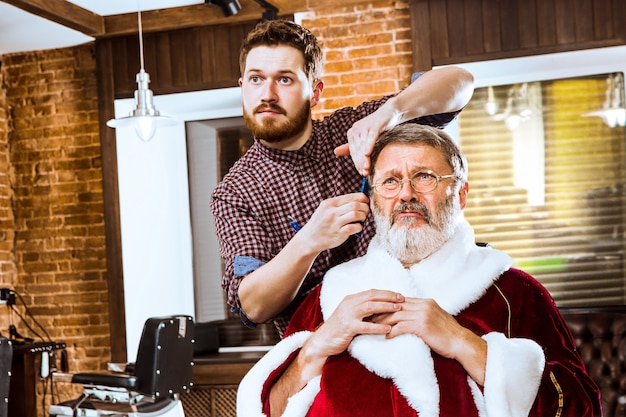 L'homme senior en costume de père Noël raser son maître personnel au salon de coiffure avant Noël