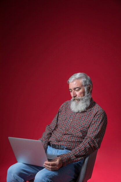 Homme senior déprimé à l&#39;aide de l&#39;ordinateur portable sur fond rouge