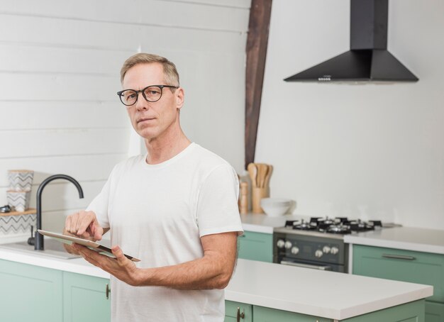 Homme senior moderne tenant sa tablette dans la cuisine