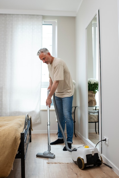 Homme senior plein coup passant l'aspirateur sur le sol