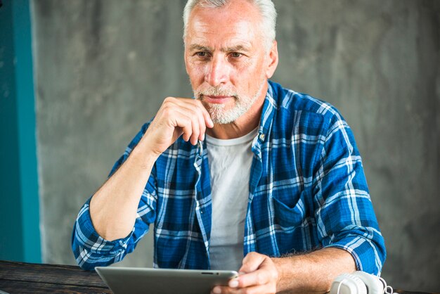 Homme senior réfléchie tenant une tablette numérique