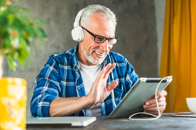 Homme senior souriant, disant bonjour sur tablette numérique