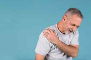 Photo gratuite homme senior stressé avec douleur à l'épaule sur fond bleu