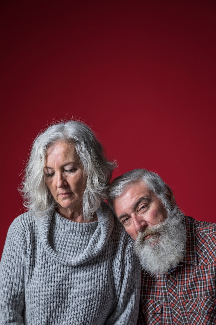 Photo gratuit homme senior triste se penchant sur l'épaule de sa femme sur fond rouge