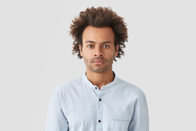 Photo gratuite homme sérieux aux cheveux bouclés, regarde avec une expression concentrée, vêtu d'une chemise blanche, écoute attentivement