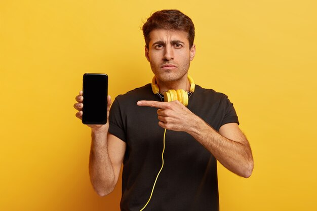 Photo gratuite un homme sérieux et confiant montre un appareil de téléphone intelligent moderne avec écran de maquette