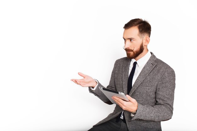 Homme sérieux en costume gris parle de quelque chose tenant la tablette dans son bras