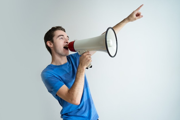 Photo gratuite homme sérieux criant dans le mégaphone et pointant loin