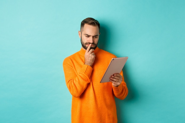 Homme sérieux réfléchissant et regardant l'écran de la tablette numérique, la lecture des médias sociaux,