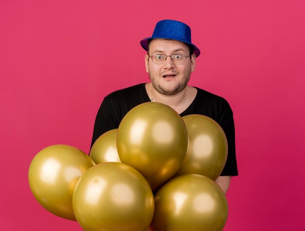 Un homme slave adulte excité dans des lunettes optiques portant un chapeau de fête bleu tient des ballons à l'hélium