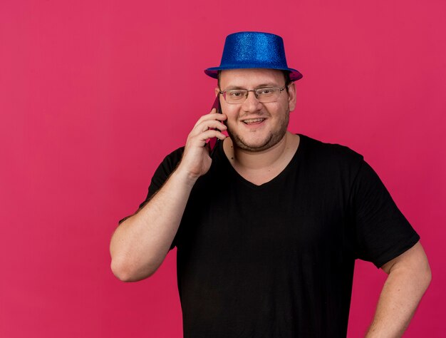 Photo gratuite homme slave adulte souriant dans des lunettes optiques portant un chapeau de fête bleu parle au téléphone