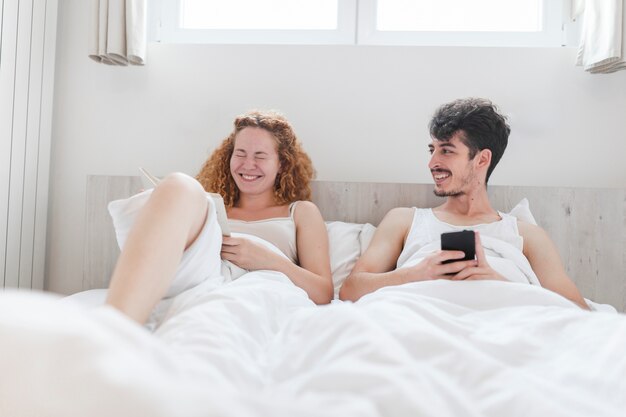 Homme avec smartphone en regardant sa femme souriant sur le lit