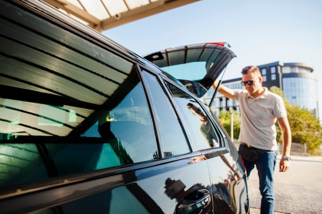 Homme soulevant la porte du coffre d'une voiture noire