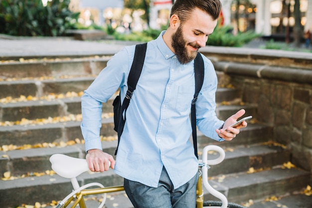 Homme souriant à l&#39;aide de smartphone près de vélo