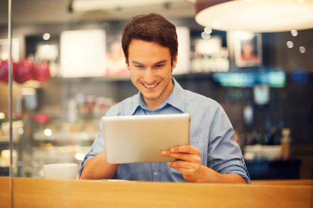 Homme souriant à l'aide de tablette numérique au café