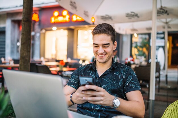 Homme souriant à l&#39;aide de téléphone portable dans un café