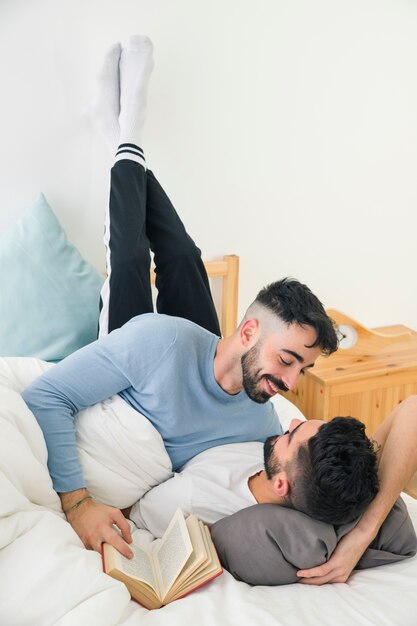 Homme souriant aimant son petit ami allongé sur le lit avec sa jambe sur le mur