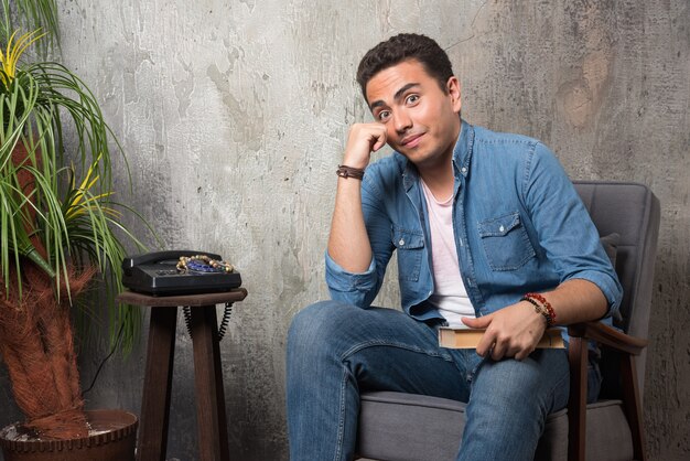 Homme souriant assis sur une chaise avec un livre sur fond de marbre. Photo de haute qualité