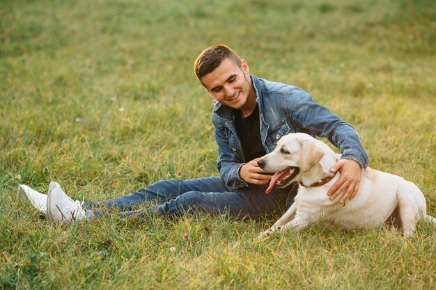 Homme souriant, assis sur l&#39;herbe avec son chien labrador dans le parc
