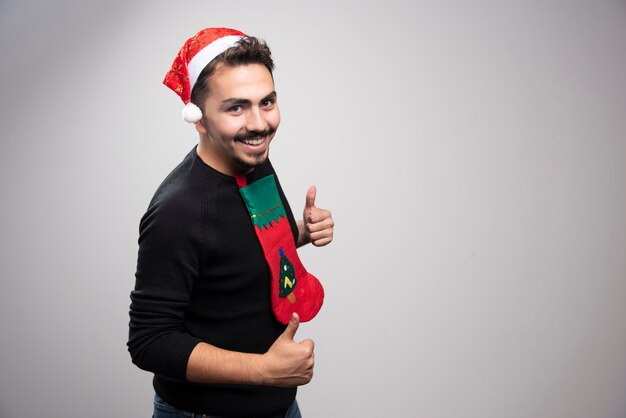 Homme souriant au chapeau du père Noël montrant les pouces vers le haut.