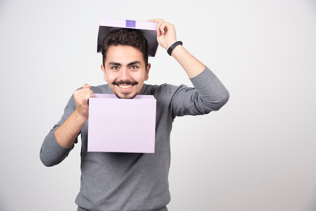 Homme Souriant Avec Une Boîte Violette Ouverte Sur Un Mur Blanc.