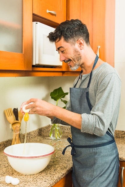 Photo gratuite homme souriant casser un oeuf dans le grand bol blanc