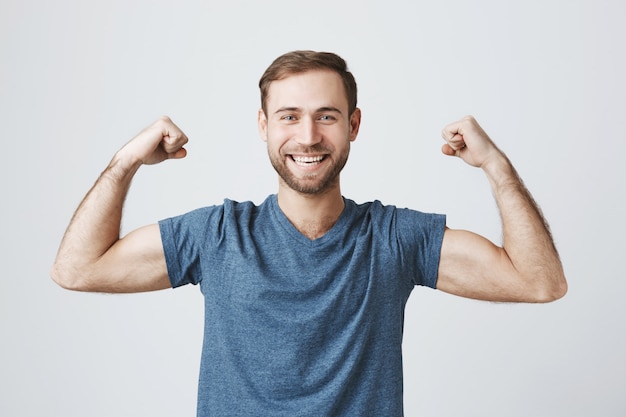 Homme souriant confiant, entraînement dans une salle de sport, flex biceps forts, montrer les muscles