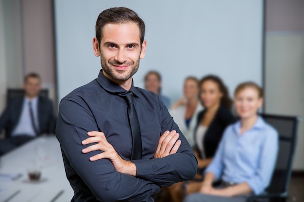 Photo gratuite homme souriant avec le costume assis à une table avec des collègues derrière