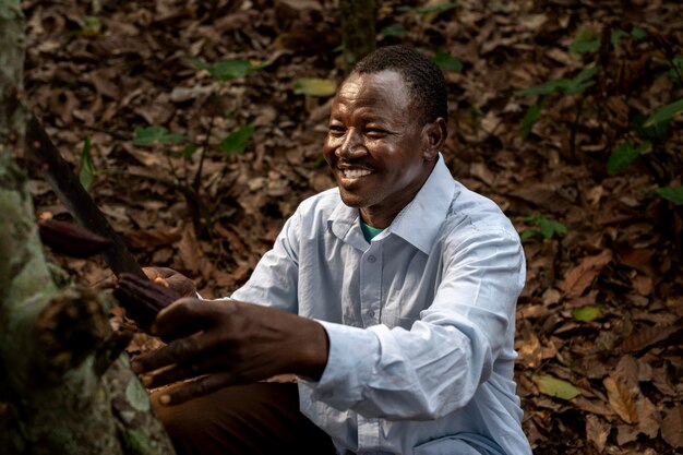 Homme souriant de coup moyen cueillant des fèves de cacao