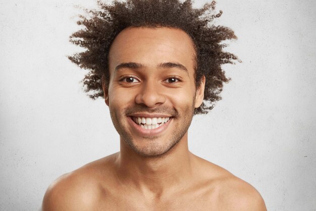 Un homme souriant heureux émotionnel a une apparence attrayante, une coiffure afro touffue, des dents blanches même