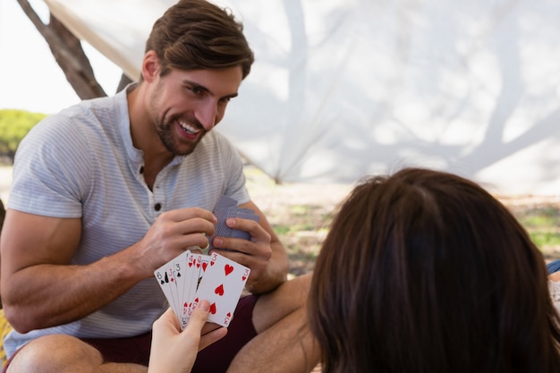 Homme souriant jouant aux cartes avec femme dans la tente