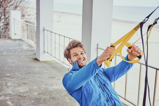 Un homme souriant et joyeux fait des exercices à l'extérieur en utilisant des bandages spéciaux.