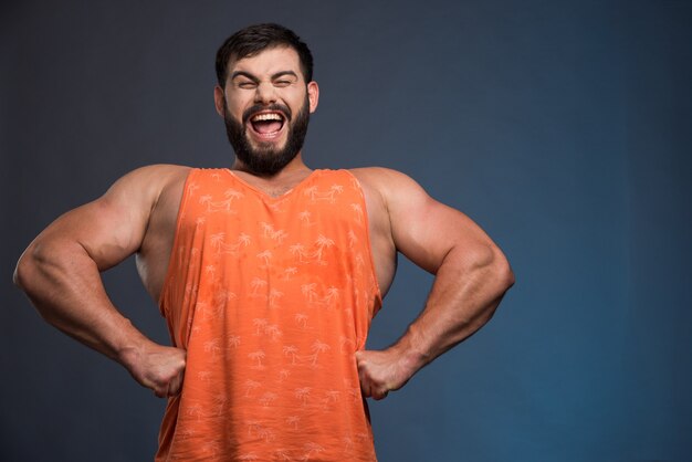 Homme souriant montrant ses muscles sur un mur bleu foncé.