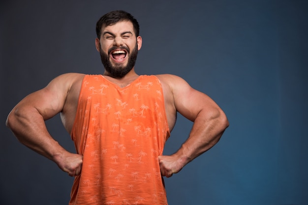 Homme souriant montrant ses muscles sur un mur bleu foncé.