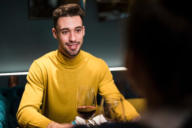 Homme souriant et personne assise à table avec des verres de vin