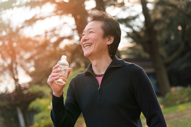 Photo gratuite homme souriant de plan moyen avec une bouteille d'eau