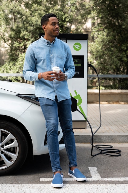 Homme souriant plein coup attendant que la voiture se recharge