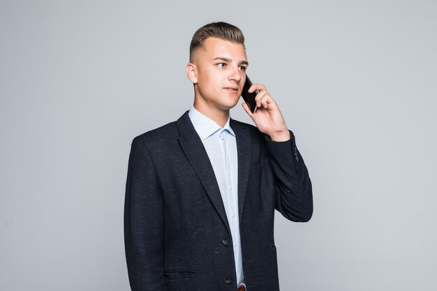 Homme souriant posant avec téléphone portable habillé en veste sombre en studio isolé sur mur gris