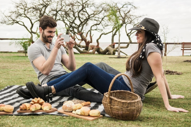 Homme souriant prenant la photo de sa petite amie lors d&#39;un pique-nique dans le parc