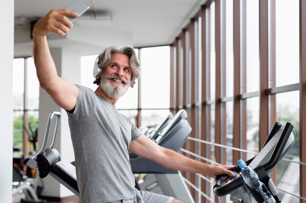 Homme souriant prenant des selfies au gymnase