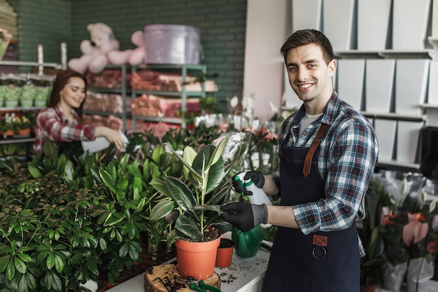 Homme souriant, pulvérisation de plantes au centre de jardinage