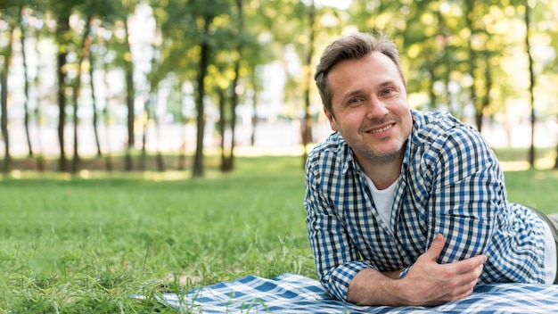Homme souriant en regardant la caméra allongée sur une couverture dans le parc